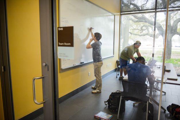 studnets working in a team room, one is writing on white board.