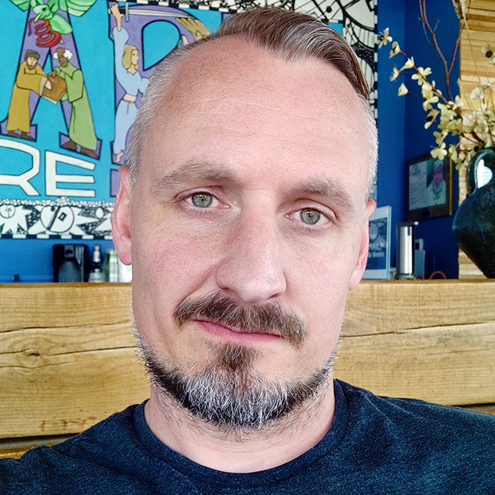 Jason Jamersom headshot. He is in a blue tshirt with artwork in the background.