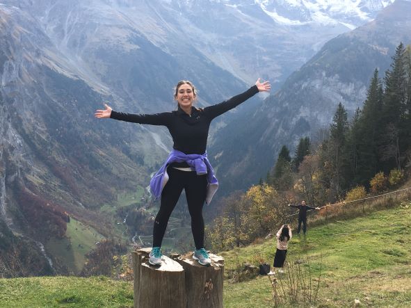 Female student stands on rock in front of mountains.