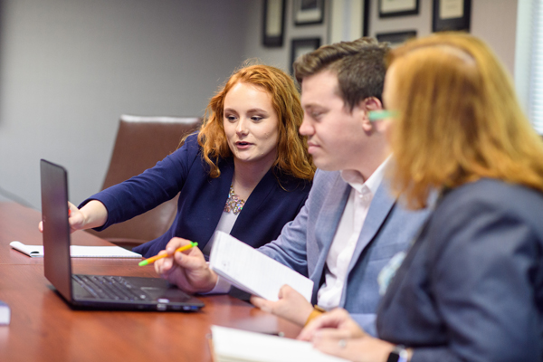 Three people at conference table, one is pointing at a laptop screen.