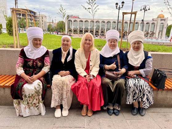 Wearing traditional Kyrgyz attire—beldemchi (a wrap-around skirt) and chyptama (a fitted vest with roots in nomadic culture)—women from Bishkek pose with the author in the city center. These garments reflect centuries-old traditions of craftsmanship, practicality, and cultural identity in Kyrgyzstan. Women wearing traditional Kyrgyz attire—beldemchi (a wrap-around skirt) and chyptama (a fitted vest with roots in nomadic culture)