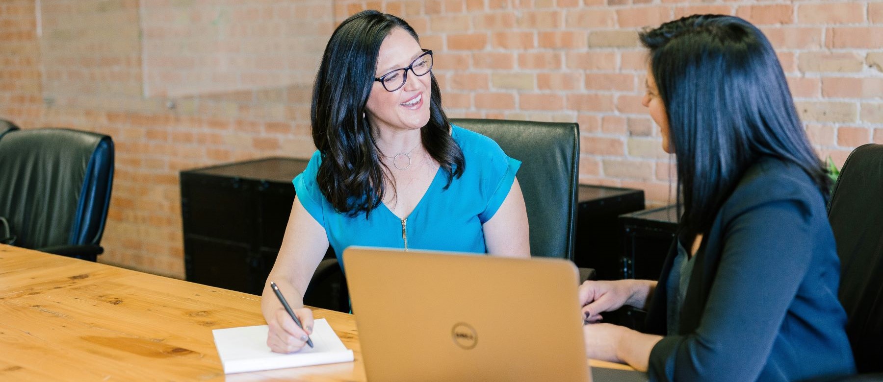 two women discuss something in front of a laptop computer