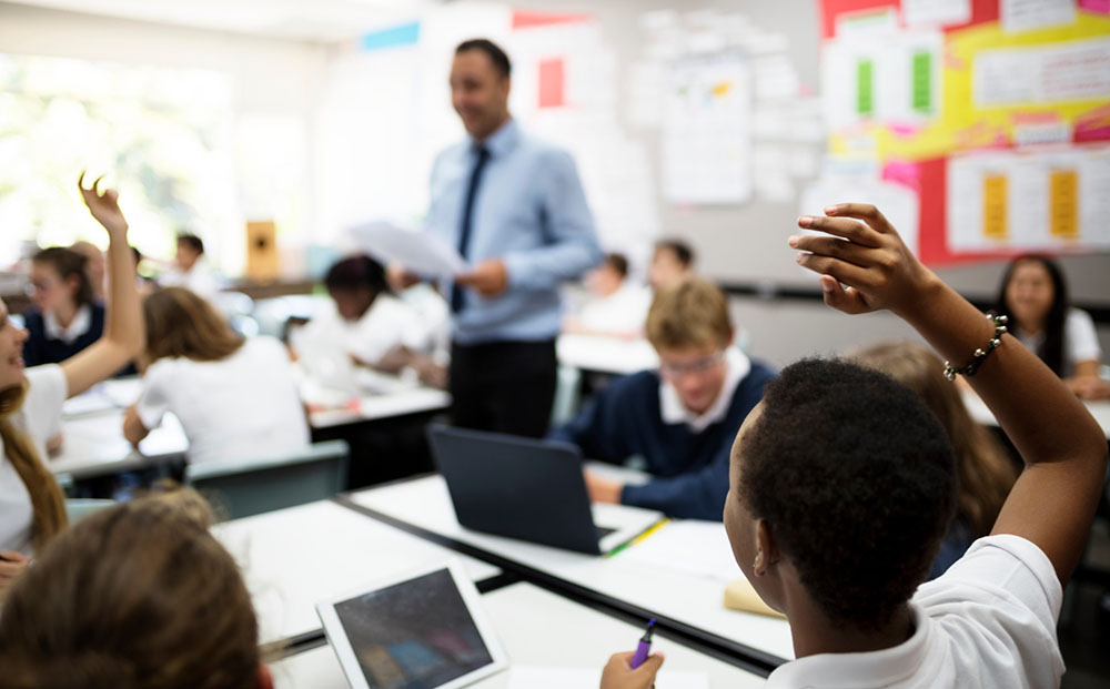 male teacher with students raising their hands