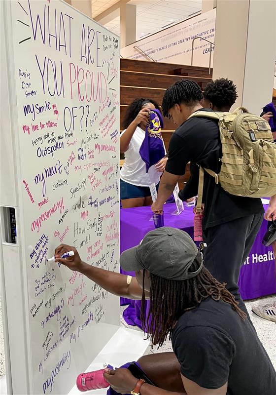 students write what they are proud of on a whiteboard at the trash your insecurities event